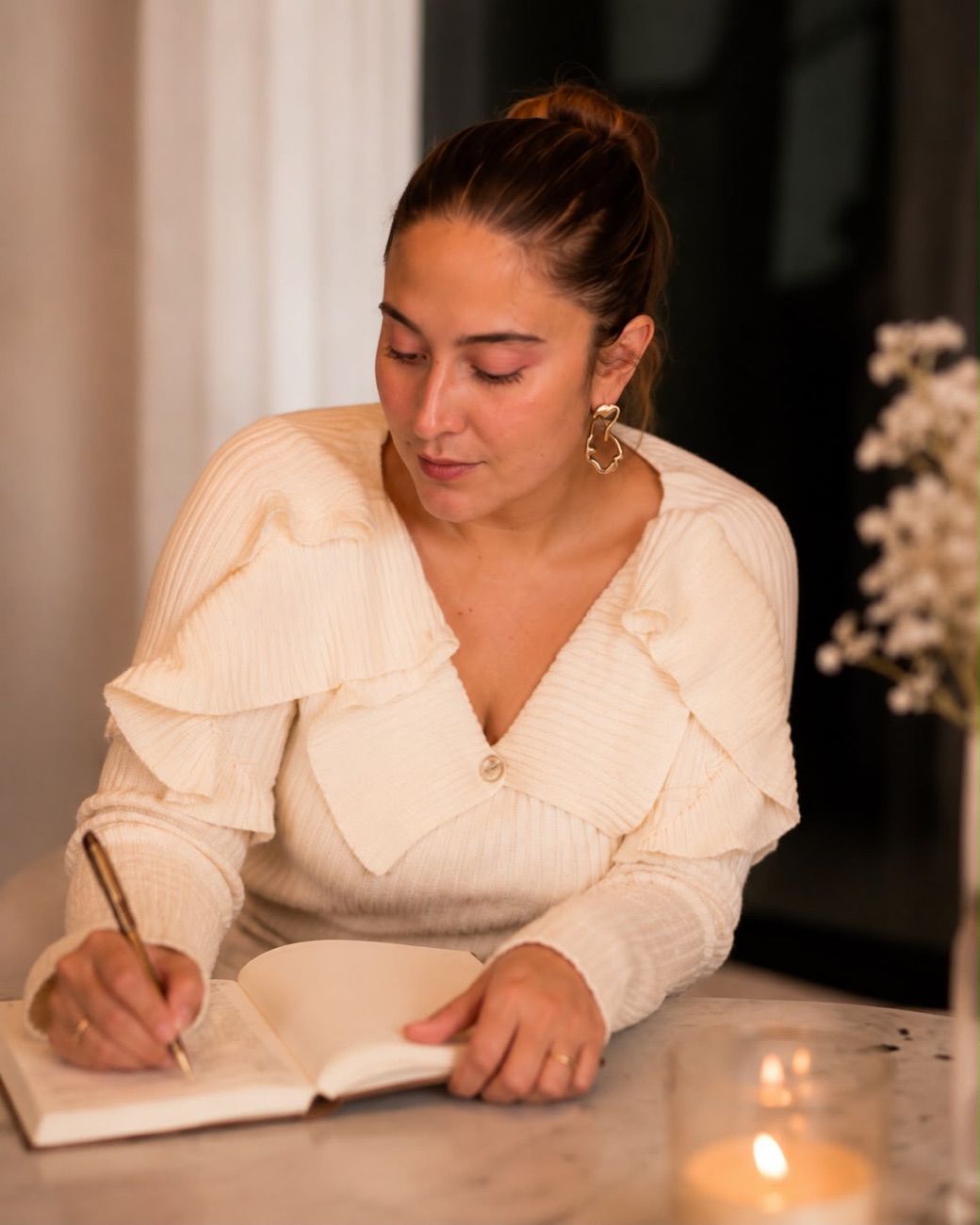 Andrea Ortega escribiendo en un diario junto a una vela, sobre superficie de mármol.